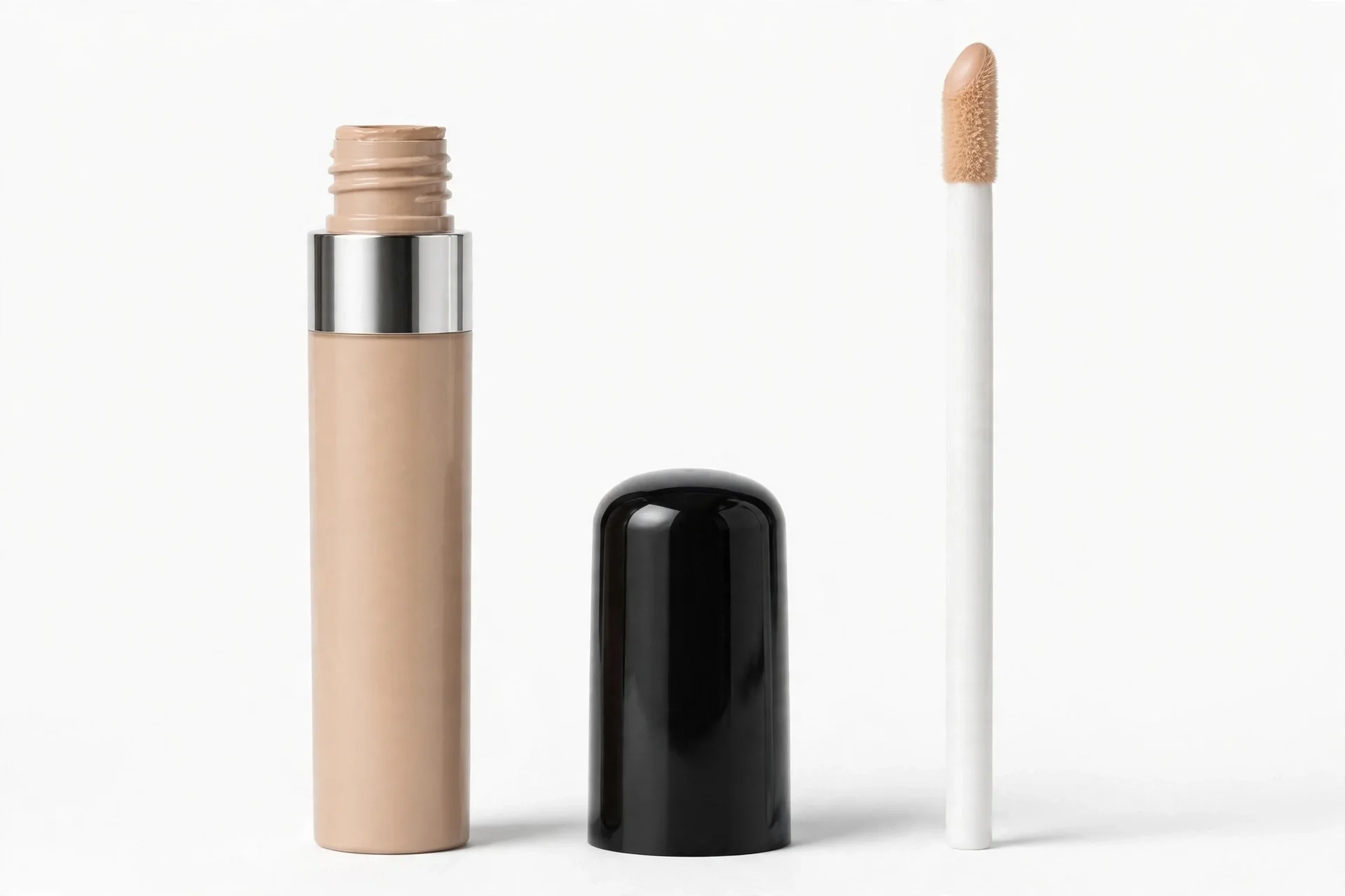 Beige concealer tube with a silver band, a glossy black cap beside it, and a tall white applicator wand with a beige tip