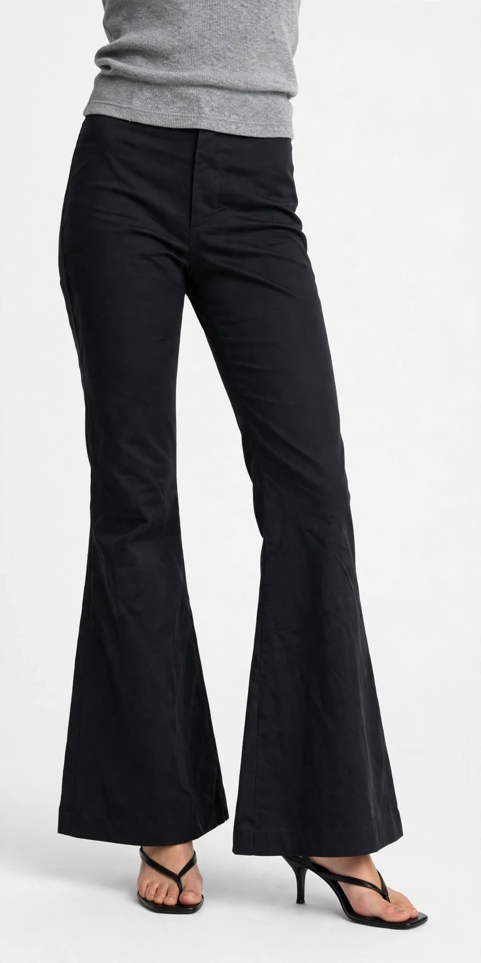 Black bootcut flared pants that widen below the knee, worn with a grey cropped top and black heeled thong sandals