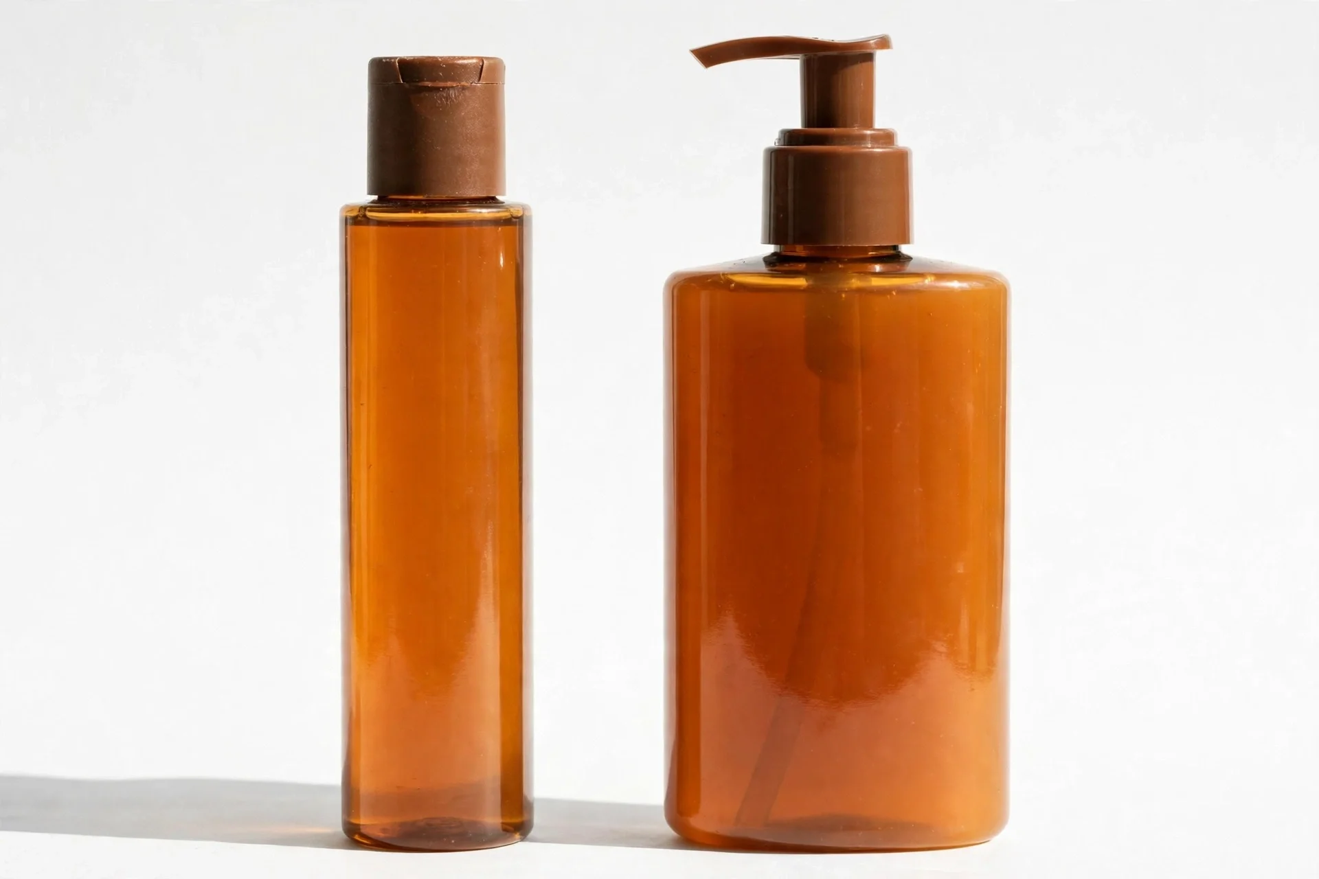 Two amber bodycare bottles side by side, a slim cylinder with a brown cap and a larger pump bottle