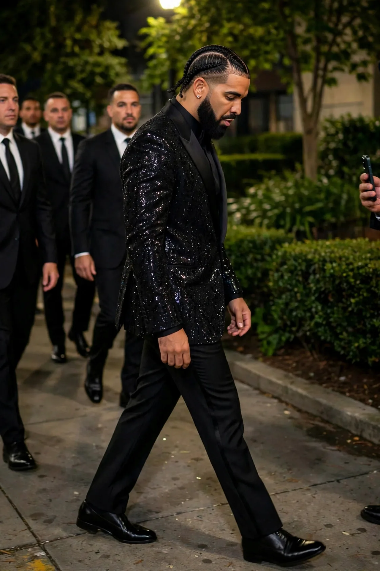 Drake walking at night in a sparkling black tuxedo, with suited men behind him