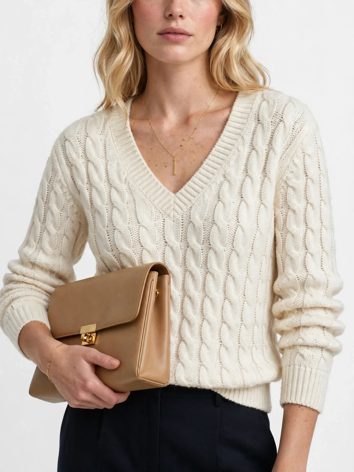 Cream off-white V-neck cable-knit sweater, worn with dark trousers and a tan clutch