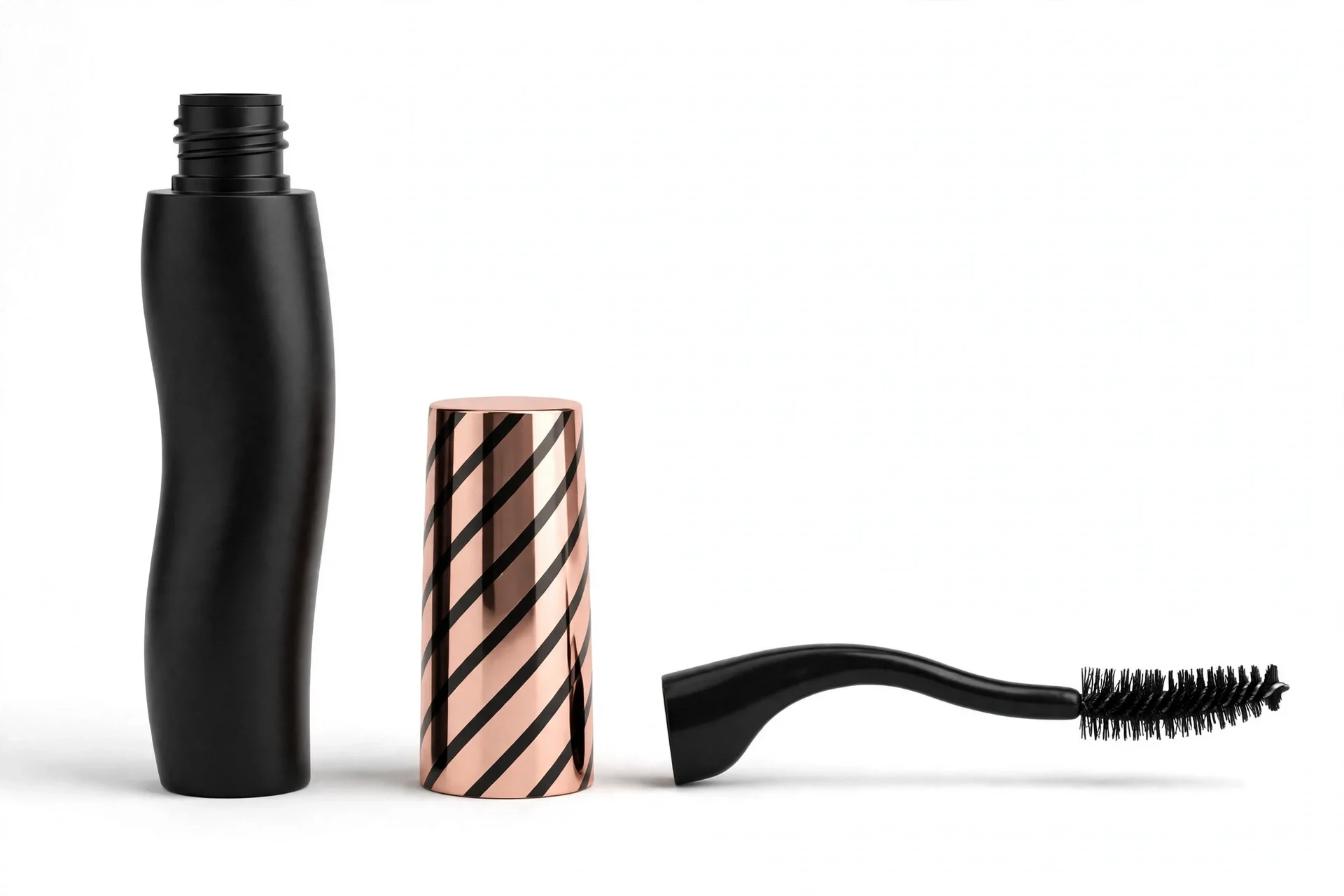 Black curvy mascara tube next to its rose-gold striped cap and black spiky curved wand
