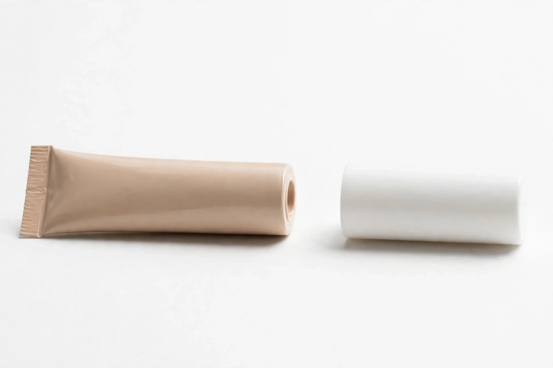 Beige concealer tube beside a plain white cylindrical cap on a white background
