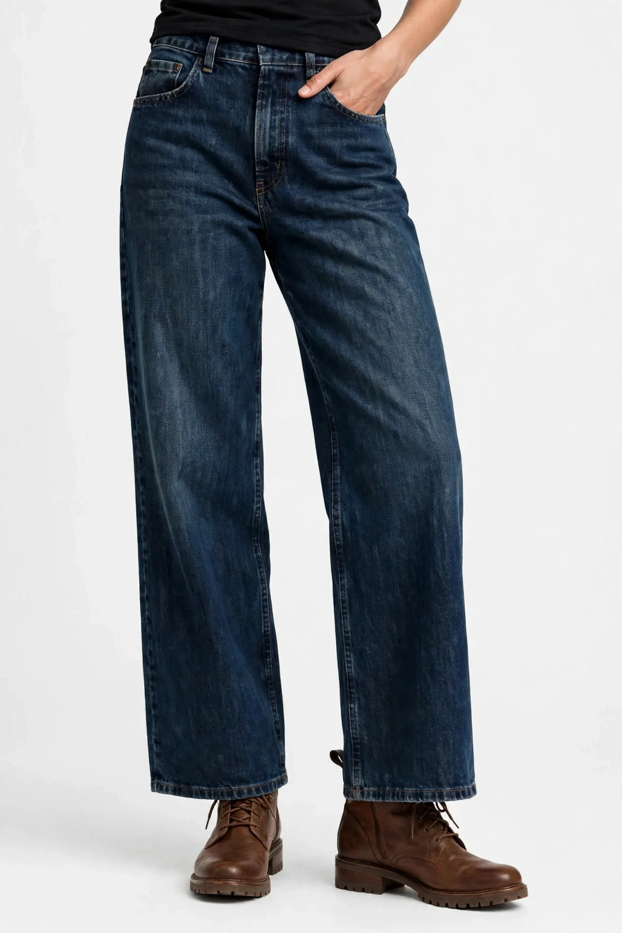 Model's lower torso and legs in dark-wash straight wide-leg jeans, one hand in a pocket, wearing brown boots