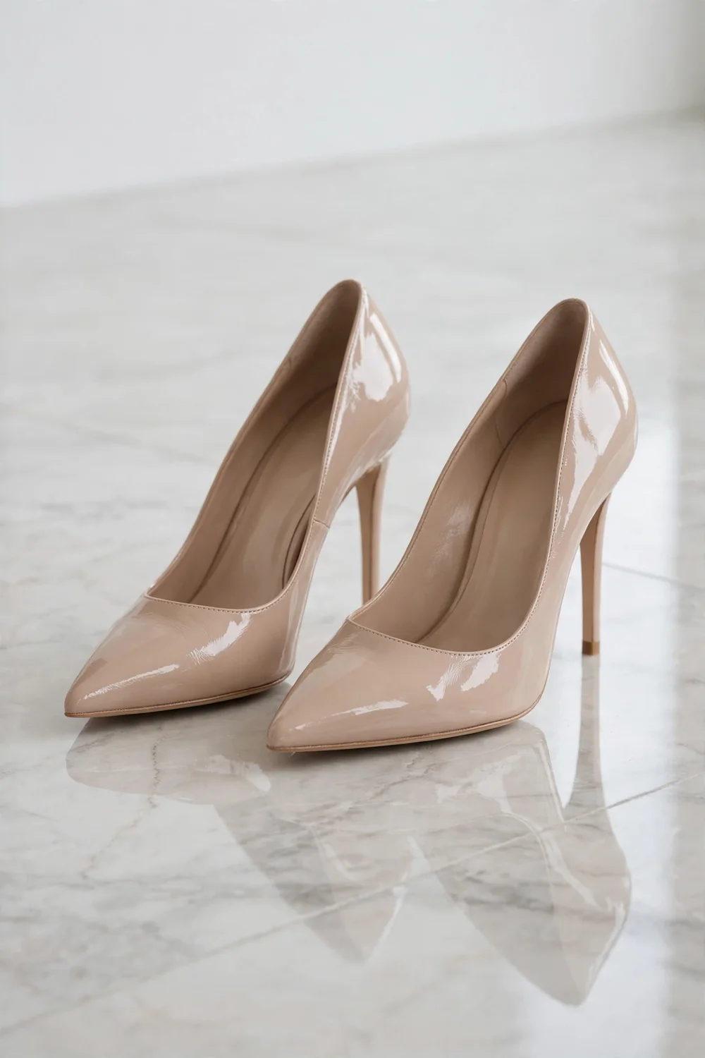 A pair of pointed-toe nude patent pumps on a polished marble floor