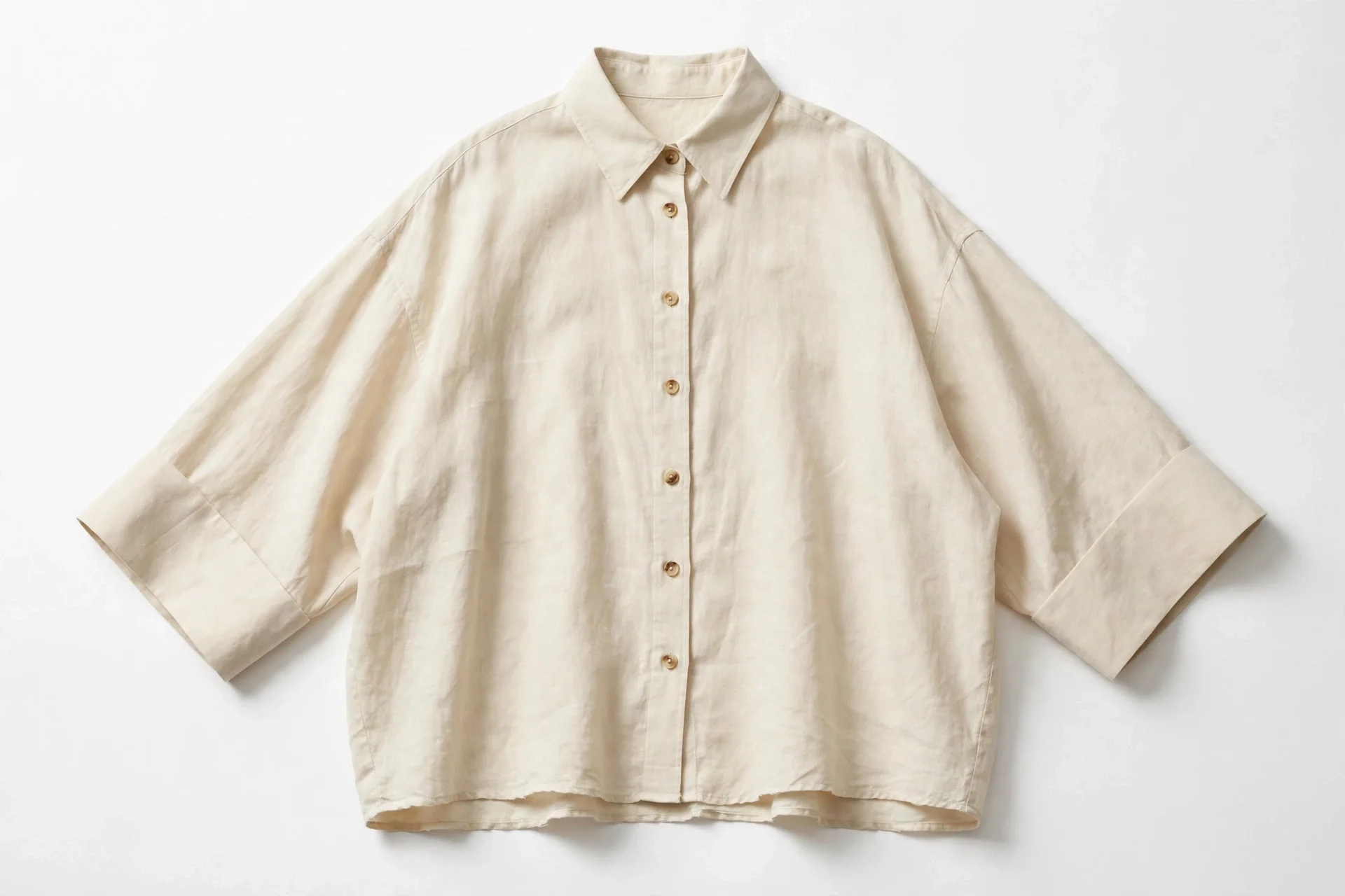 Flat photo of a cream beige oversized button-down shirt with pointed collar, full button front, dropped shoulders and wide three-quarter sleeves with broad cuffs