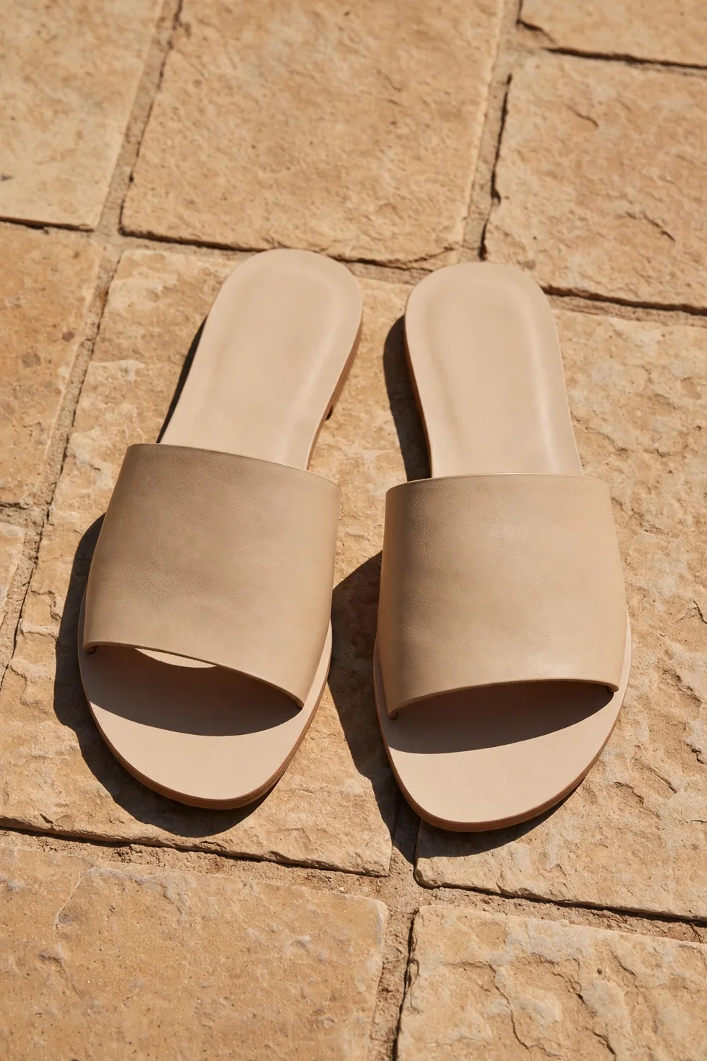 Simple neutral flat sandals on warm stone tiles